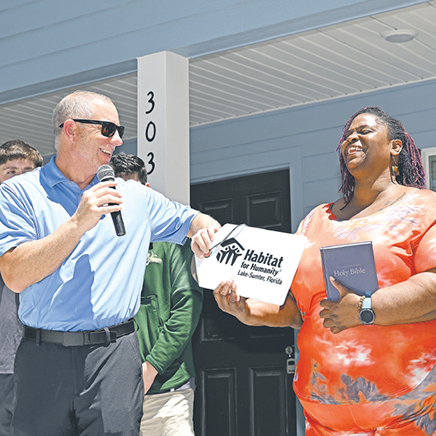 Picture of symbolic large key being presented to a family during Habitat for Humanity of Lake & Sumter Counties home dedication ceremony.