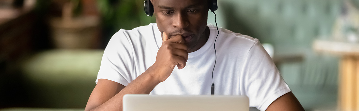 Focused African American student wearing headphones studying online using laptop.