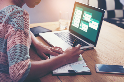 Woman writing on notepad and looking at laptop.